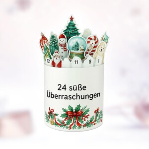 May include: A white Christmas advent calendar with 24 slots, each featuring a festive illustration. The top has cutouts of a Christmas tree, snowman, and candy cane. The base is decorated with holly and a red bow.