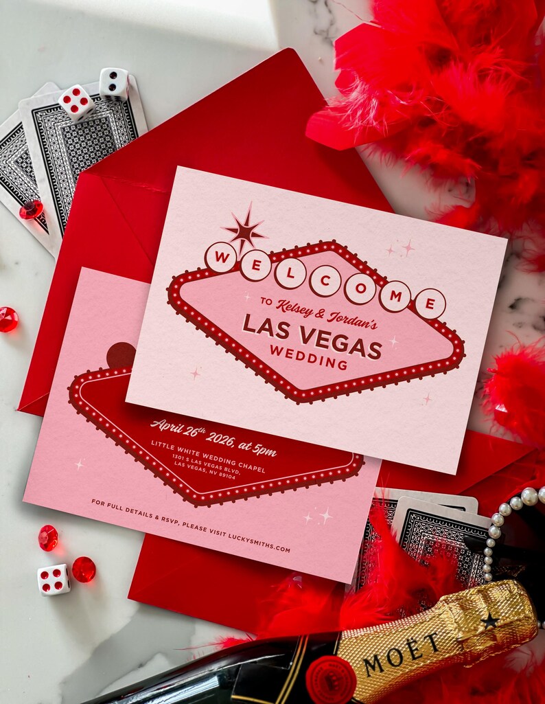 May include: Pink and red Las Vegas wedding invitations with a retro sign design. The invitations include the text "Welcome to Kelsey & Jordan's Las Vegas Wedding" and event details. Playing cards, dice, and a bottle of champagne are also in the image.