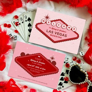 May include: Two pink Las Vegas wedding invitations with red text and a retro design, surrounded by playing cards, dice, and red feather boa. One invitation reads "Welcome to Kelsey & Jordan's Las Vegas Wedding."