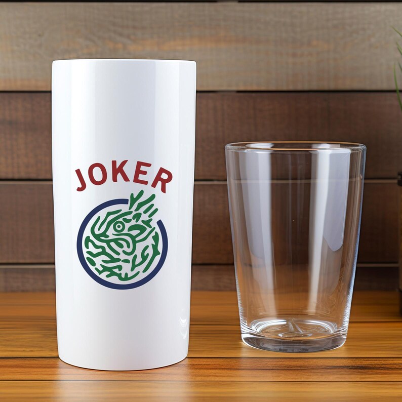 K&ouml;nnte beinhalten: Ein wei&szlig;er Becher mit dem Wort "JOKER" in roter Schrift und einer gr&uuml;n-blauen Grafik. Ein klares Glas befindet sich neben dem Becher. Beide stehen auf einer Holzoberfl&auml;che.