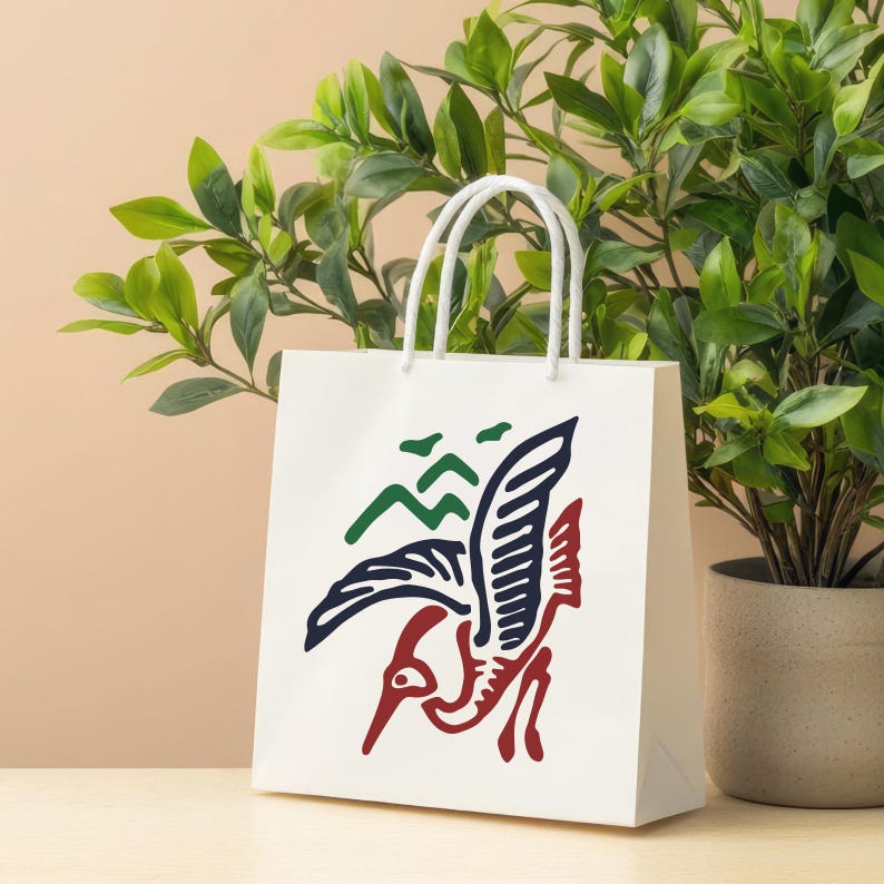 K&ouml;nnte beinhalten: Eine wei&szlig;e Papiereinkaufstasche mit einem Vogeldesign in Marineblau, Rot und Gr&uuml;n. Der Vogel ist im Flug dargestellt, mit einem langen Schnabel und ausgebreiteten Fl&uuml;geln. Die Tasche hat wei&szlig;e Kordelgriffe und steht auf einer hellen Oberfl&auml;che.