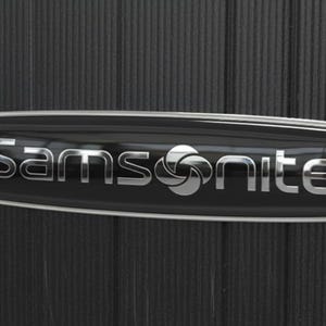 Pode incluir: Uma mala preta com uma superfície texturizada de riscas verticais. Centrado na parte frontal encontra-se um emblema retangular preto brilhante com uma borda prateada, exibindo o nome da marca Samsonite em letras prateadas e um ícone.