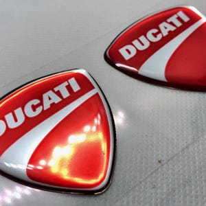 May include: Two red and white 3D resin stickers with the word "DUCATI" in white lettering.