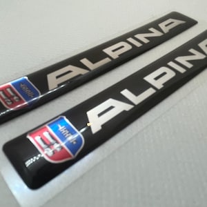 May include: Two black and silver "ALPINA" decals with a blue, red, and white shield logo.