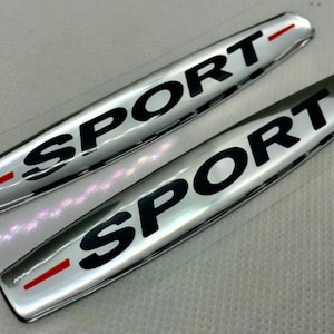 May include: Two silver car badges with a red stripe and the word "SPORT" in black lettering.