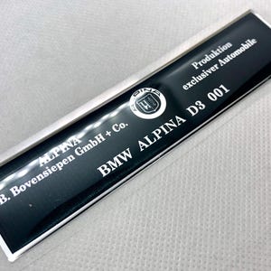 May include: A black and silver metal plaque with the text "ALPINA B. Bovensiepen GmbH + Co. BMW ALPINA D3 001 Produktion exklusiver Automobile".