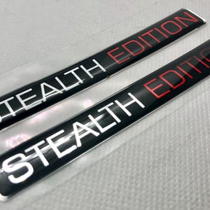 Puede incluir: Dos calcomanías negras y plateadas con el texto "STEALTH EDITION" en letras blancas y rojas.