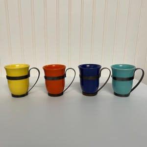 May include: Four ceramic mugs with metal bands around the middle. The mugs are yellow, orange, blue, and teal.