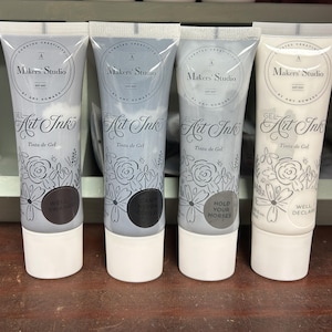 May include: Four bottles of Makers' Studio Gel Art Ink in various colors. The bottles are labeled with the brand name and the words "Gel Art Ink" and "Tinta de Gel". The bottles are decorated with a floral design.