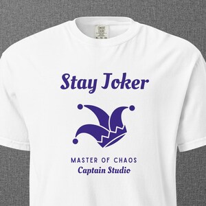 May include: White t-shirt with a purple jester hat graphic and the words "Stay Joker" above the graphic. Below the graphic, the text reads "MASTER OF CHAOS" and "Captain Studio".