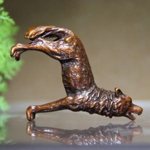 May include: A bronze-colored sculpture of a wolf in a dynamic pose, with its front legs raised and its body arched. The wolf's fur is detailed, and its mouth is slightly open. The sculpture is likely made of metal.