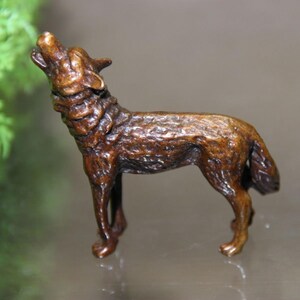 May include: A bronze-colored wolf figurine in a howling pose. The sculpture has detailed fur texture and is standing on four legs with its head raised and mouth open. The figurine is a decorative item.
