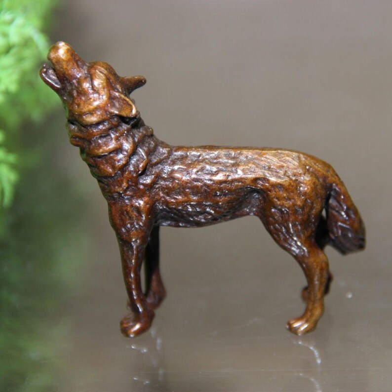 May include: A bronze-colored wolf figurine in a howling pose. The sculpture has detailed fur texture and is standing on four legs with its head raised and mouth open. The figurine is a decorative item.