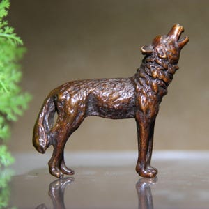 May include: A bronze-colored wolf figurine in a howling pose. The sculpture has detailed fur texture and is standing on all fours with its head raised and mouth open. The figurine is a decorative item.
