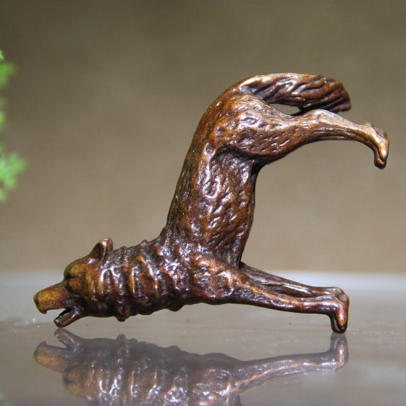 May include: A bronze sculpture of a wolf in a dynamic pose, arching its back and extending its front leg. The sculpture has a textured surface and a rich, brown patina. The wolf's head is detailed with an open mouth, suggesting a howl or a bark.