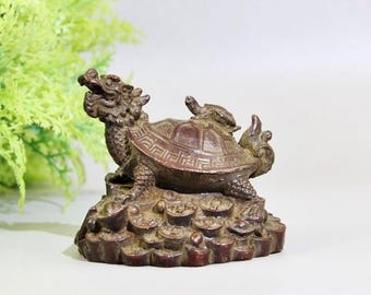 May include: A bronze-colored figurine depicting a dragon-turtle hybrid. The sculpture features intricate details, including a dragon head, a turtle shell, and a base of coins. The figurine is a symbol of longevity and prosperity.