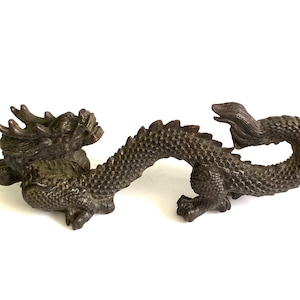 Puede incluir: Figura de dragón de color bronce, con escamas detalladas y cola enroscada. El dragón está en una pose dinámica, con la cabeza levantada y la boca abierta. La figura es probablemente de metal y es un objeto decorativo.