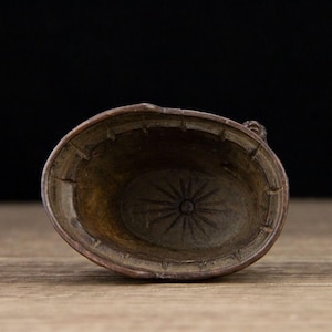 Puede incluir: Un cuenco ovalado de color bronce con un dise&ntilde;o de estrella en la base. El cuenco tiene un borde texturizado y est&aacute; sobre un fondo oscuro. El cuenco es probablemente un objeto decorativo o funcional.