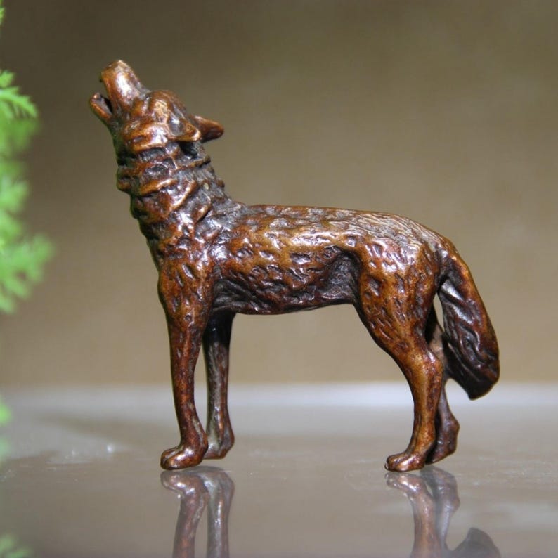 May include: A detailed bronze-colored wolf figurine in a howling pose. The sculpture features intricate details of the wolf's fur and anatomy. The wolf stands on four legs with its head tilted back, mouth open in a howl.