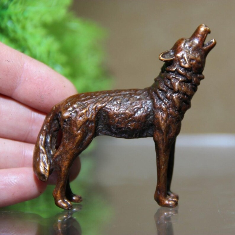 May include: A bronze-colored wolf figurine in a howling pose. The sculpture has detailed fur texture and is standing on four legs with its head raised and mouth open. The figurine is a decorative item.
