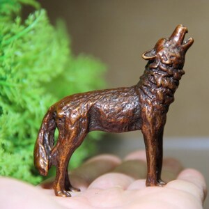 May include: A bronze-colored wolf figurine in a howling pose. The sculpture has detailed fur texture and is standing on four legs with its head raised and mouth open. The figurine is a decorative item, likely for display.
