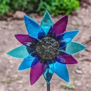 May include: A colorful glass flower with teal, purple, and blue petals. The center of the flower is made of dark glass with iridescent glitter.