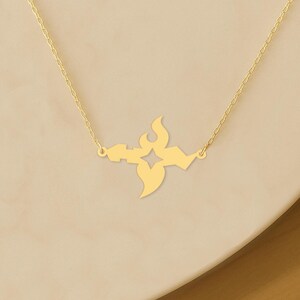 May include: A gold-colored necklace featuring a stylized, symmetrical pendant. The pendant has a central diamond shape, flanked by flame-like and curved elements. The necklace chain is delicate and gold-toned, creating a minimalist and elegant design.