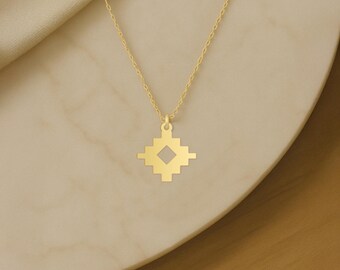 May include: A gold-colored necklace with a geometric pendant. The pendant is a square shape with a smaller square cut out in the center, and a chain is attached to the top. The necklace is displayed on a light-colored surface.