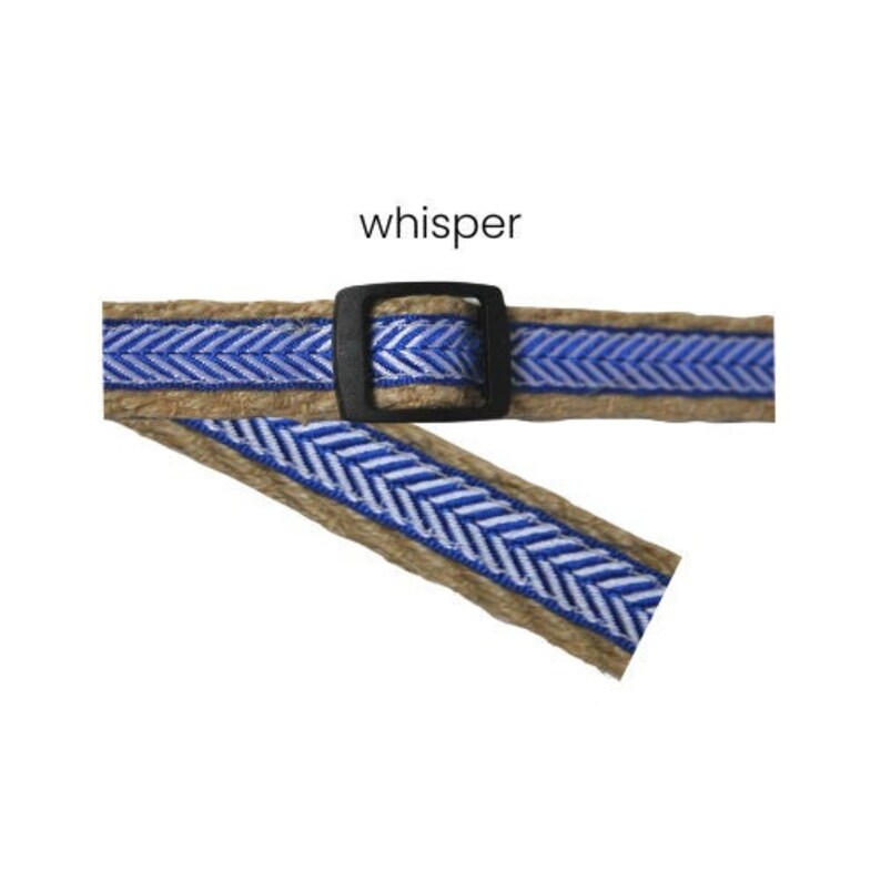 Puede incluir: Primer plano de un cintur&oacute;n con hebilla negra. El cintur&oacute;n tiene una base marr&oacute;n natural con un patr&oacute;n de chevr&oacute;n azul y blanco. La palabra "whisper" est&aacute; impresa encima del cintur&oacute;n.