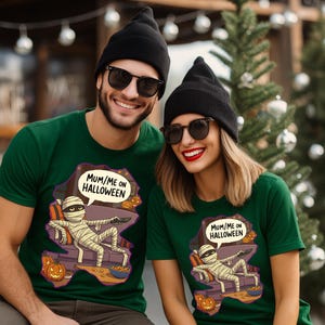Puede incluir: Dos personas con camisetas verdes a juego con un diseño de Halloween. El diseño presenta una momia relajándose en un sofá con el texto "MUM/ME ON HALLOWEEN". Ambos llevan gorros negros y gafas de sol.