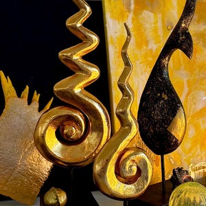 Puede incluir: Tres esculturas abstractas de color dorado con un diseño en espiral sobre una superficie negra. Las esculturas están hechas de un material liso y brillante y tienen una forma orgánica única.