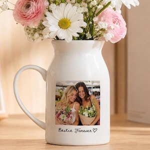 May include: A white ceramic pitcher-style mug featuring a printed photograph of two individuals holding bouquets of flowers. Below the image, the text "Bestie Forever" is written in black script, accompanied by a small hand-drawn heart symbol.