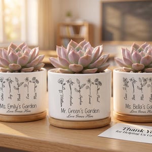 May include: Three white ceramic succulent planters with wooden bases, each featuring a different teacher's name and the text "Love Grows Here." The planters hold light pink succulents. A card reads "Thank You for Helping Us Grow."
