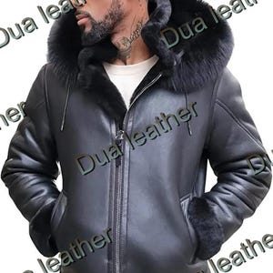 Puede incluir: Chaqueta de cuero negra con capucha y puños forrados de piel. La chaqueta tiene cierre de cremallera y dos bolsillos delanteros. El texto "Dua leather" es visible. Una prenda de abrigo elegante.