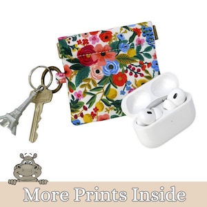 May include: A white AirPods case with two white earbuds, a floral print pouch, and keys with a silver Eiffel Tower charm. The pouch features a colorful floral pattern with red, pink, and blue flowers. The text "More Prints Inside" is at the bottom.