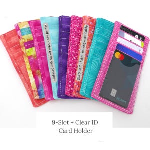 May include: A collection of colorful fabric card holders, each with a different pattern and color, including pink, purple, and turquoise. One holder displays credit cards. The text "9-Slot + Clear ID Card Holder" is visible.