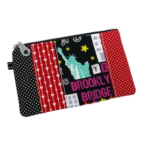 May include: A rectangular zippered pouch with a patchwork design. The pouch features panels of black polka dots, red hearts, and a black panel with the Statue of Liberty and the words "BROOKLYN BRIDGE". The right panel is red with white polka dots.