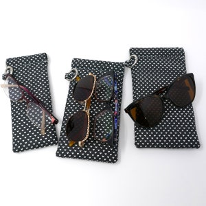 May include: Three black eyeglass cases with white heart patterns. Each case has a silver ring and a pair of glasses inside. The glasses are different styles and colors.