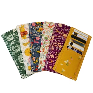 May include: A collection of fabric card wallets in various floral patterns. The wallets are open, revealing card slots. Colors include green, yellow, navy, and purple. Each wallet has a unique floral design, with visible stitching.
