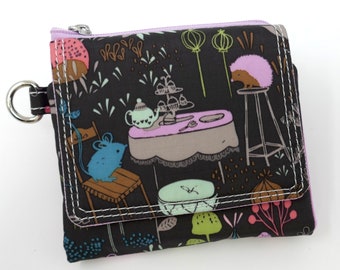 May include: A black wallet with a whimsical print featuring a tea party scene with a mouse, hedgehog, and teapot. The wallet has a purple zipper, white stitching, and a silver key ring.