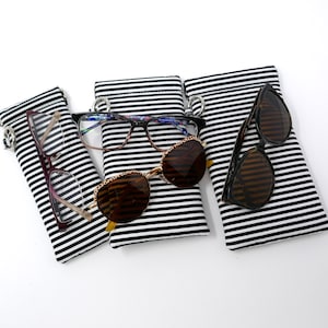 May include: Four striped black and white fabric cases for glasses. Three cases have glasses inside. The glasses include a pair of reading glasses, a pair of sunglasses, and a pair of prescription glasses.