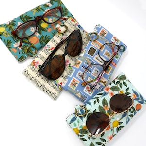 May include: Four different fabric eyeglass cases with glasses inside. The cases are made of cotton fabric with various patterns, including musical notes, postage stamps, and floral designs. The glasses are a mix of reading glasses and sunglasses.