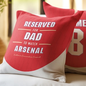 May include: Two red throw pillows with white trim. One pillow has the text "RESERVED FOR DAD TO WATCH ARSENAL" and the other pillow has the number "8" in white.