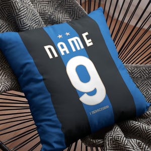 Könnte beinhalten: Blau-schwarzes, gestreiftes Kissen mit dem Wort "NAME" und der Zahl "9" in Weiß. Der Text "I NERAZZURRI" ist unten auf dem Kissen in Weiß gedruckt.