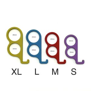 Pode incluir: Quatro tamanhos diferentes de um abridor de maçanetas de porta de cor amarela, azul, vermelha e roxa. Os tamanhos são etiquetados como XL, L, M e S. O abridor de maçanetas tem três furos, cada um com um diâmetro diferente. Os diâmetros são etiquetados em milímetros.