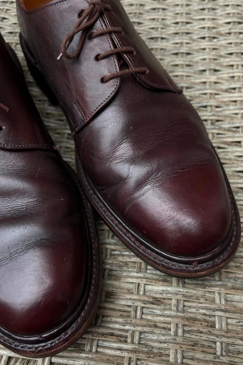 May include: A pair of burgundy leather dress shoes with brown laces. The shoes have a rounded toe and a stitched sole. The leather has a polished finish and shows subtle variations in color.