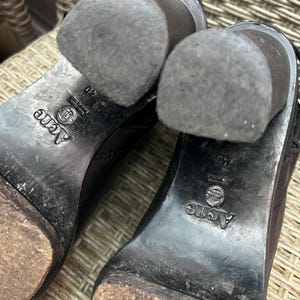 May include: Close-up of the soles of two black leather boots. The heels are worn and show signs of use. The brand name "Acne" is visible on the sole, along with the size 40.
