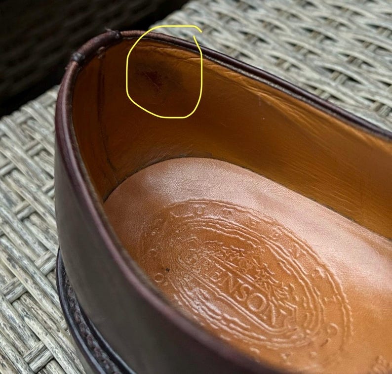 May include: Close-up of a brown leather shoe interior. The shoe's interior is tan, with a stamped logo on the insole. The shoe's exterior is a dark brown color. The shoe appears to be well-worn.