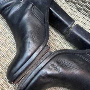 May include: Black leather boots with a high heel and a buckle detail. The boots have a worn appearance, with visible wear on the soles and heels. The heel is approximately 4 inches.