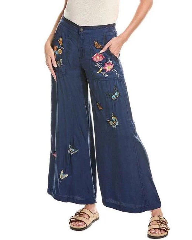 May include: Navy blue wide-leg trousers adorned with embroidered butterflies and floral patterns. The trousers have a button and zip fastening, pockets, and a loose fit. The embroidery incorporates multiple colours, enhancing the garment's decorative appeal.